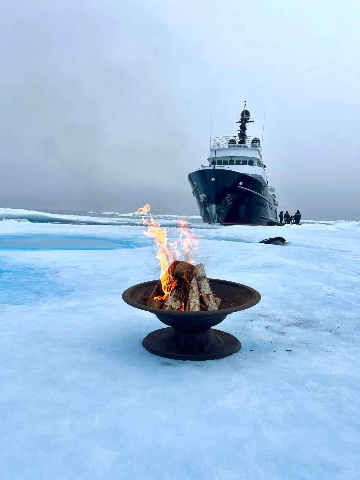 Fire bowl on the Svalbard pack ice with the expedition yacht beyond