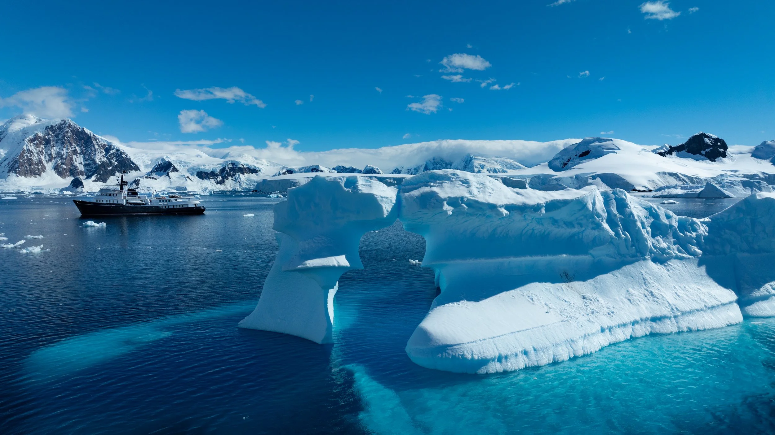 Explorer yacht among icebergs and mountains of the Antarctic Peninsula